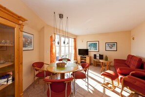 Una sala de estar con una mesa de comedor, sillas rojas, un sofá, un televisor y un aparador.