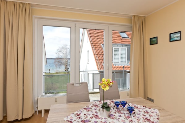 Une pièce comprenant une table, des chaises, un vase à fleurs et donnant sur un bâtiment avec un toit rouge.