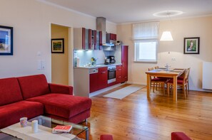 A modern living room with a red sofa, a glass coffee table, and a dining area with a wooden table and chairs.