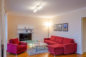 A living room with a red sofa, a glass coffee table, a flat-screen TV, and a lamp.