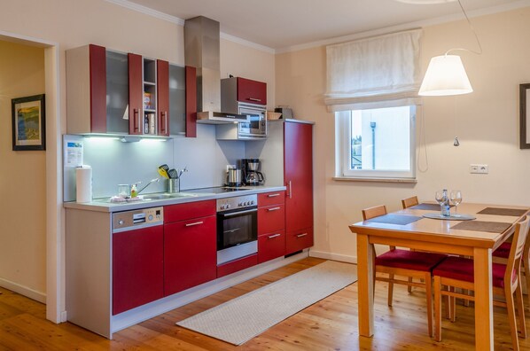 A compact kitchen with red cabinets, a microwave, and a dining area with a table and chairs.
