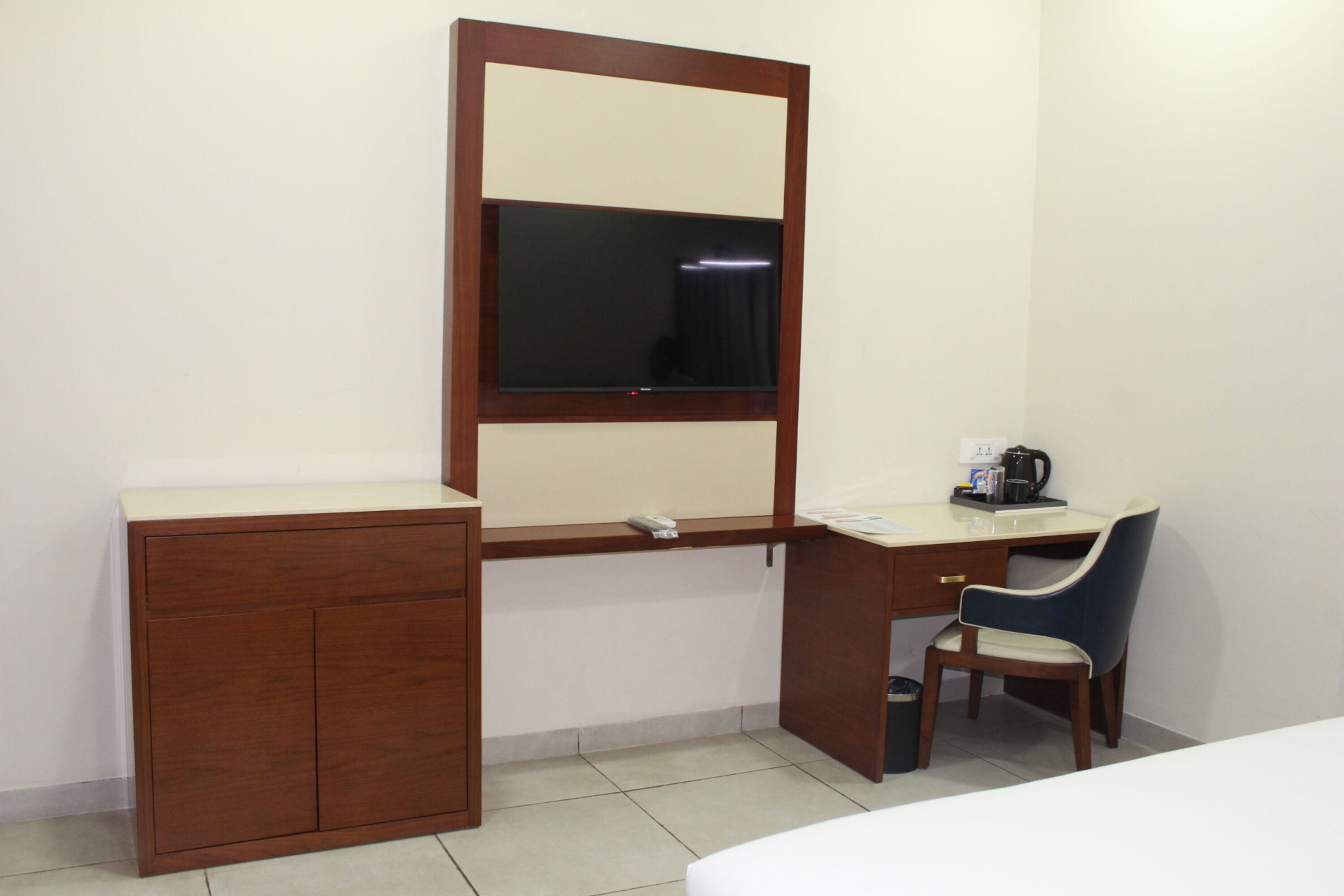 A hotel room with a wooden desk, a chair, a bed, a small cabinet, and a mirror.