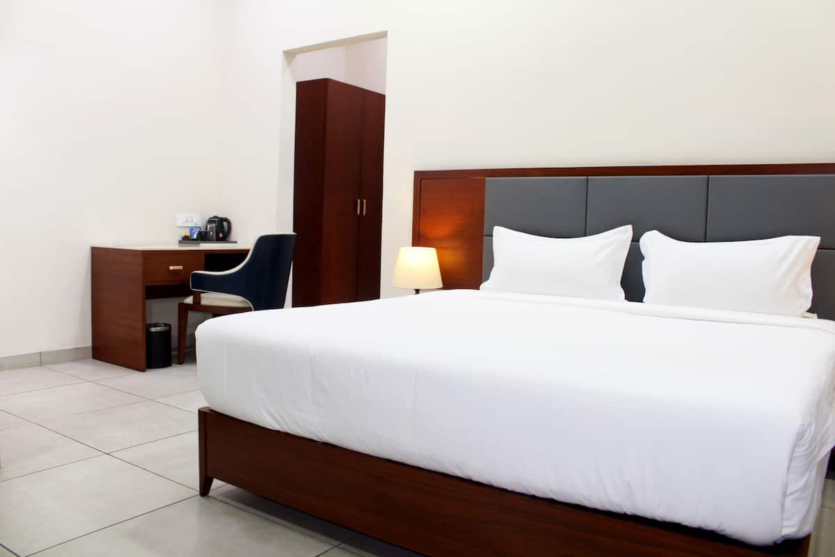 A hotel room with a large bed, a desk with a chair, a lamp, and a wardrobe.