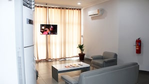 A living room with a flat-screen TV, a potted plant, a sofa, and a coffee table. - Ixoras Hotel (Kinshasa)