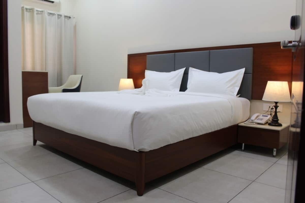 A hotel room with a large bed, bedside tables, a chair, and a bathroom with curtains.