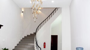 A modern staircase with a black railing, a hanging chandelier, and a fire extinguisher mounted on the wall. - Ixoras Hotel (Kinshasa)