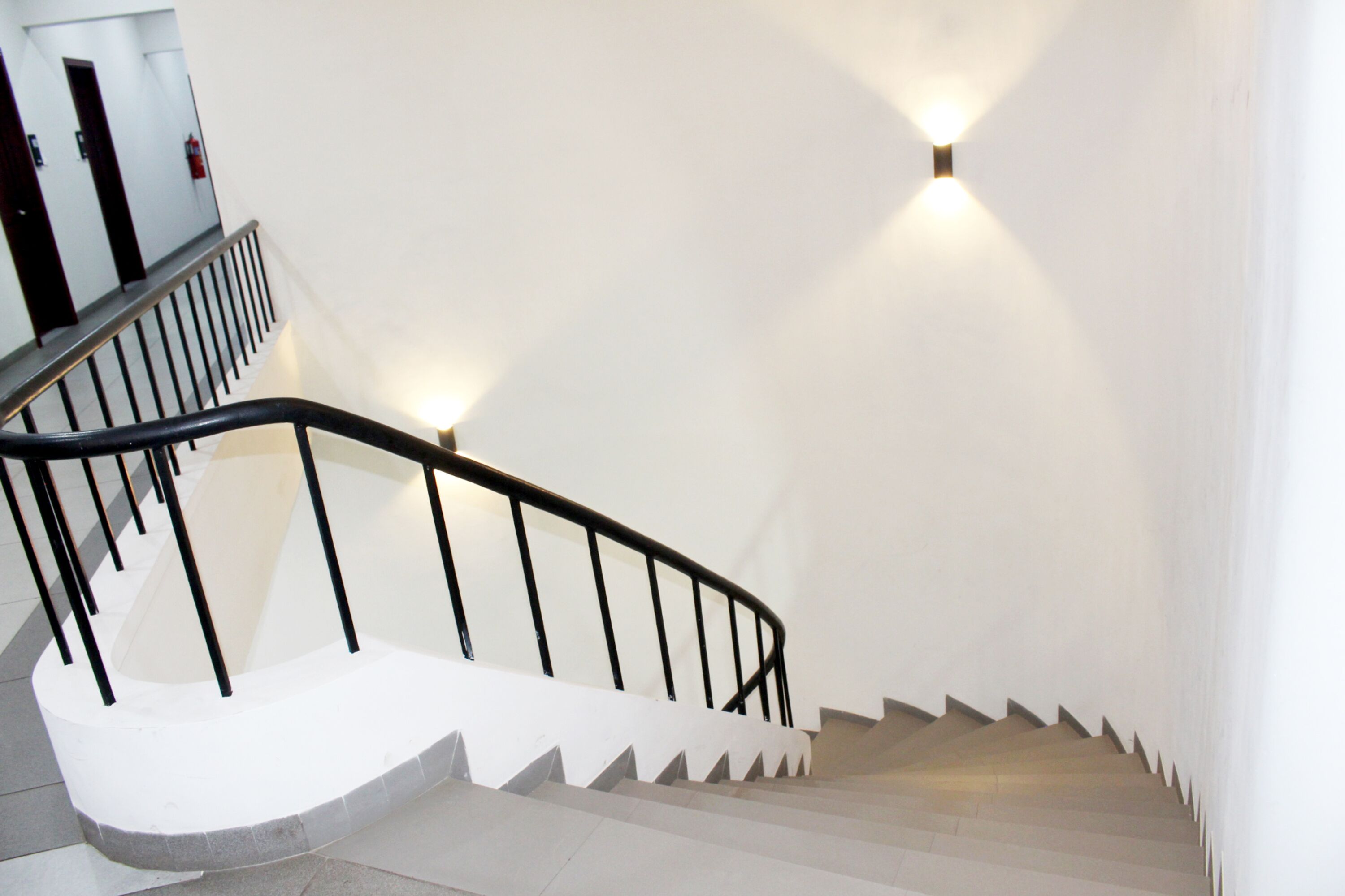 A staircase with a black railing and white steps, leading to a landing with a door and a fire extinguisher.