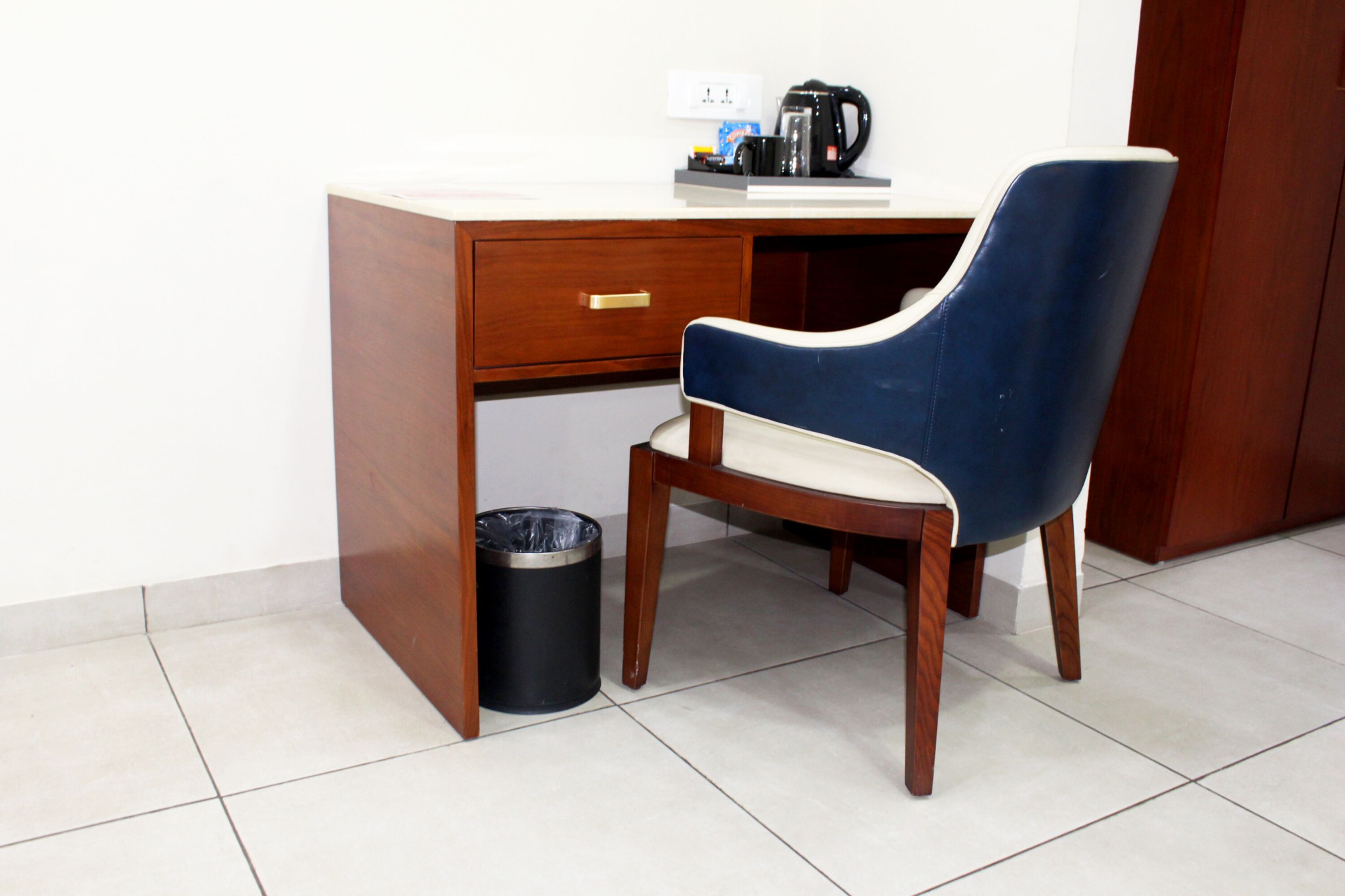 Un bureau en bois, une chaise bleue, une machine à café et une poubelle.