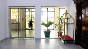 A hotel lobby with a glass door entrance, a potted plant, and a gold-colored cart. - Ixoras Hotel (Kinshasa)