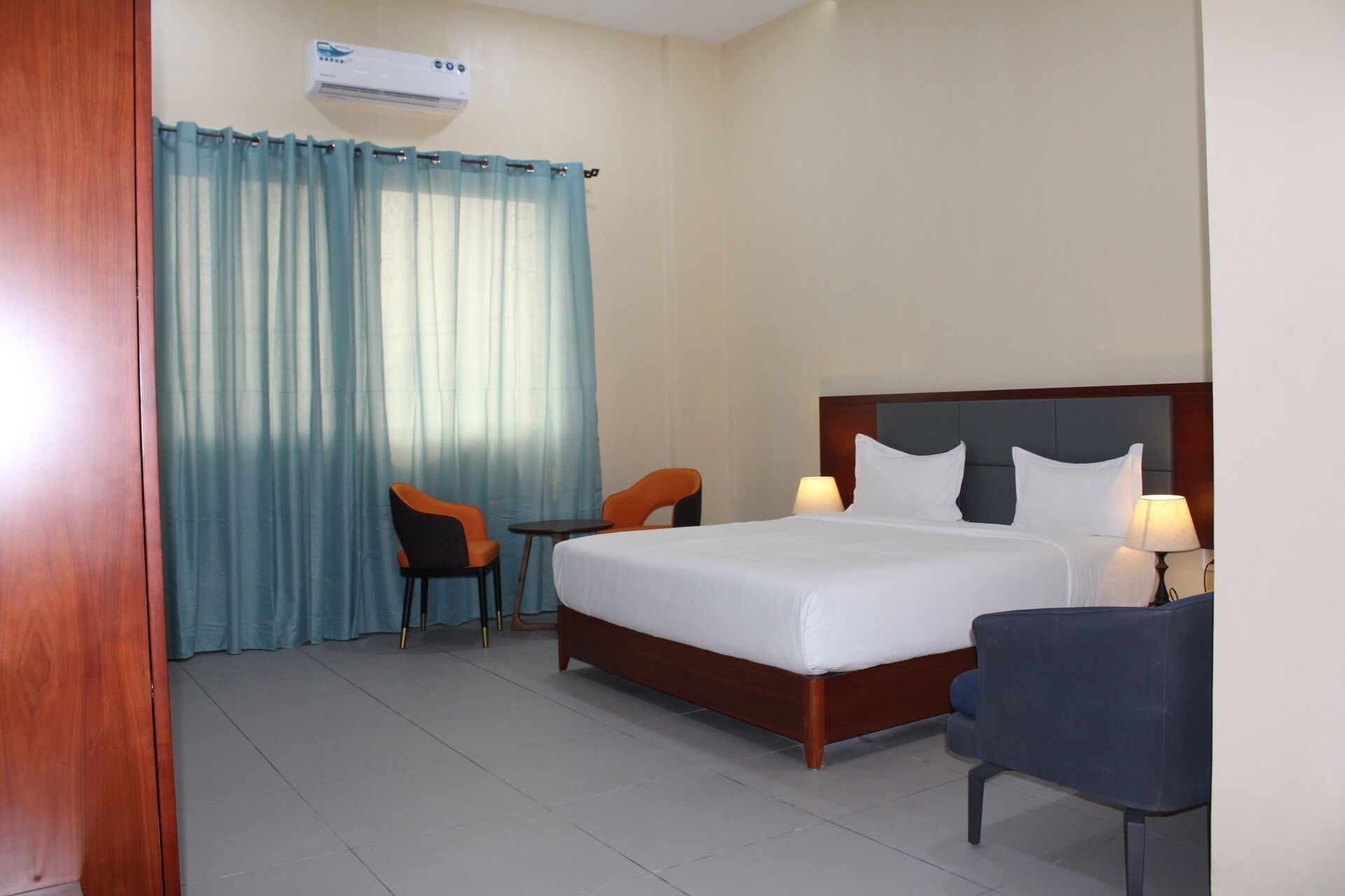 Habitación de hotel con cama, dos sillas, una mesita y ventana con cortinas.