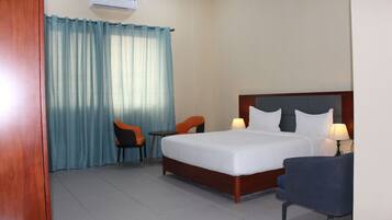 Habitación de hotel con cama, dos sillas, una mesita y ventana con cortinas.