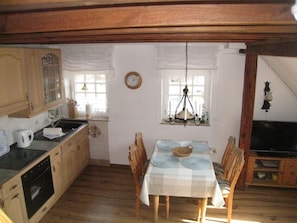 A compact kitchen with wooden cabinets, a dining table with blue placemats, and a chandelier. - Kietzspeicher App. 31 (Waren (Müritz))