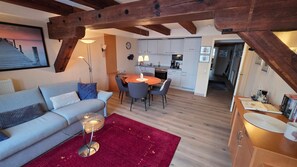 Un salon moderne avec un canapé, une table basse en verre et un tapis rouge. On y trouve également un coin cuisine avec des meubles blancs et une table à manger.