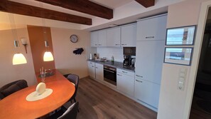 Une cuisine moderne avec des meubles blancs, un four encastré et une machine à café. On y trouve une table à manger avec des chaises et des lampes suspendues au-dessus.