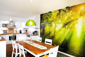 Una cocina moderna con armarios blancos, una mesa de comedor de madera y un gran mural con motivos forestales en la pared.