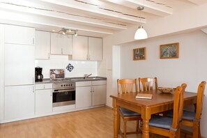A compact kitchen with white cabinets, a stove, and a dining table with wooden chairs.