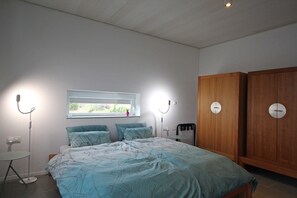 Une chambre à coucher comprenant un lit, une fenêtre, une table de chevet, une lampe sur pied et une armoire.