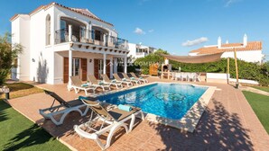 A two-story building with a swimming pool, lounge chairs, and a covered patio area. - Wonderful Villa Bellavista with Sea Views & Private Pool, Sleeps 8 (Arenal d'en Castell, Es Mercadal)