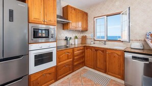 A kitchen with wooden cabinets, stainless steel appliances, and a window with a view. - Wonderful Villa Bellavista with Sea Views & Private Pool, Sleeps 8 (Arenal d'en Castell, Es Mercadal)