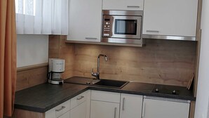 Una cocina compacta con armarios blancos, un microondas de acero inoxidable, una cafetera y un lavabo.