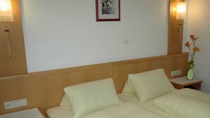 Una cama doble con dos almohadas, una mesita de noche con un florero y una lámpara de pared.
