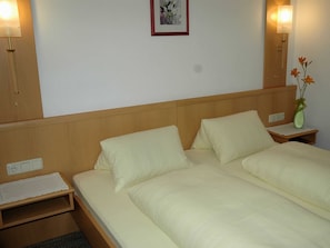 Una cama doble con dos almohadas, una mesita de noche con un florero y una lámpara de pared.