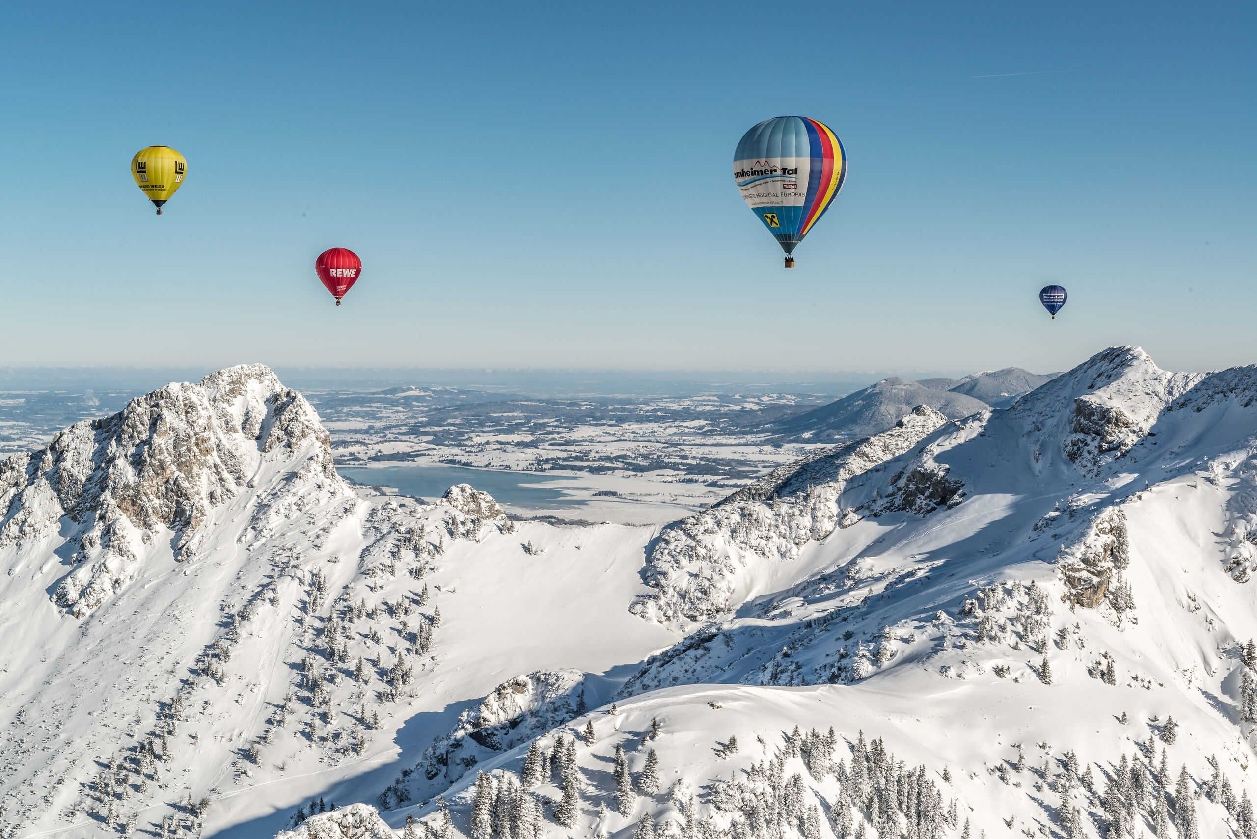 A snowy mountain landscape with multiple hot air balloons.