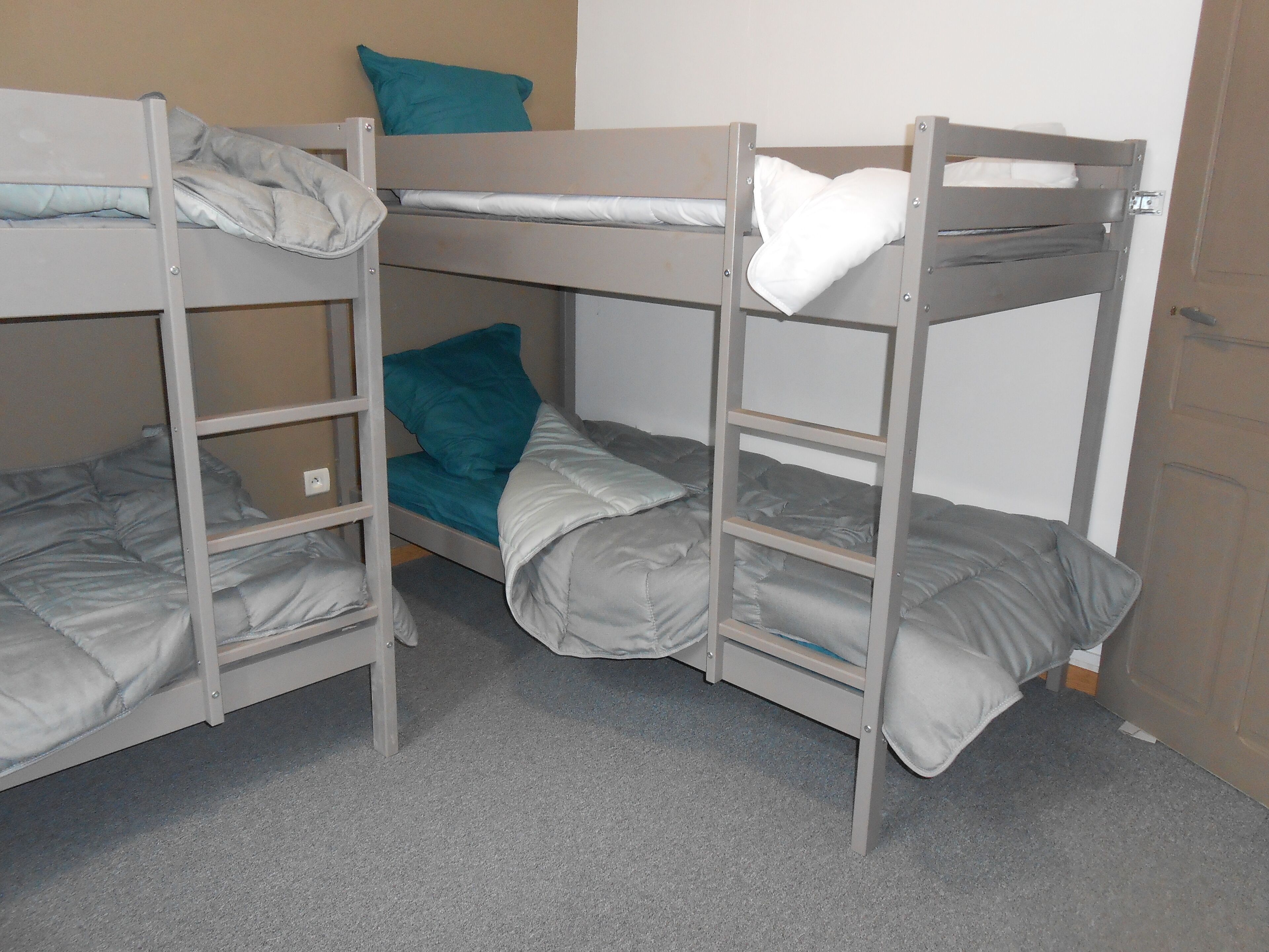 A bunk bed room with grey bedding and a teal pillow.