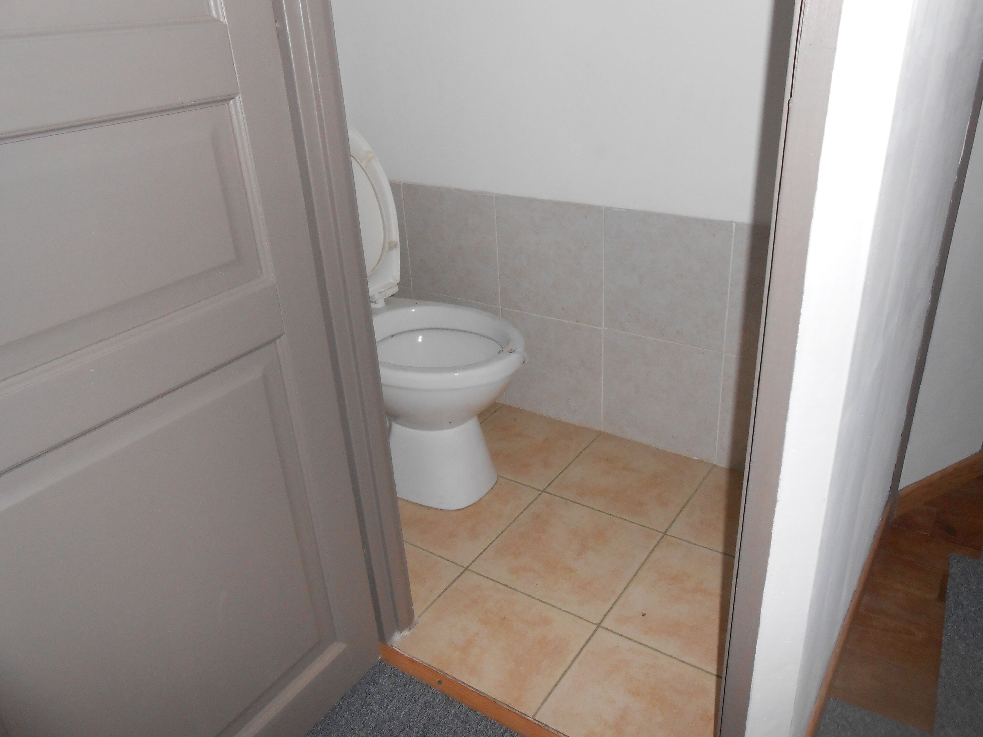 Un baño con inodoro, una puerta y suelo de baldosas.