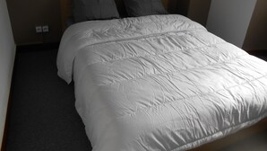 A neatly made bed with a white duvet and two pillows, a wooden headboard, and a plain wall with a power outlet. - 8-seater apartment 80 m2 (laruns)