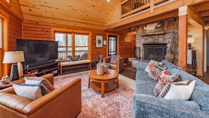 A cozy log cabin interior with a living room featuring a fireplace, a television, and comfortable seating. - Lake Cabin Luxury Near Deep Creek w/ Fire Pit (Swanton)
