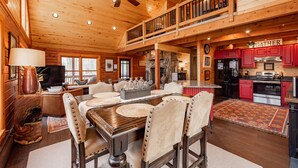 A spacious living area with a wooden ceiling, a dining table with chairs, a kitchen with red cabinets, and a balcony with a railing. - Lake Cabin Luxury Near Deep Creek w/ Fire Pit (Swanton)