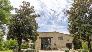 A stone building with a large glass door, outdoor seating, and a well-maintained garden.