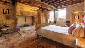 A rustic bedroom with exposed wooden beams, a large bed, a stone fireplace, and a wooden wardrobe.