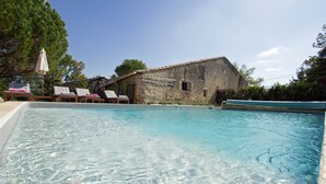A clear swimming pool with lounge chairs and a rustic stone building in the background.
