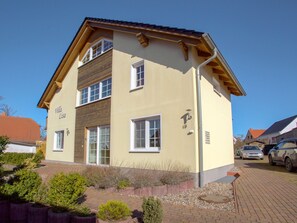 A two-story house with a beige exterior, white windows, and a wooden roof. - Vacation Apartment 4 - Villa Lisa (Glowe)