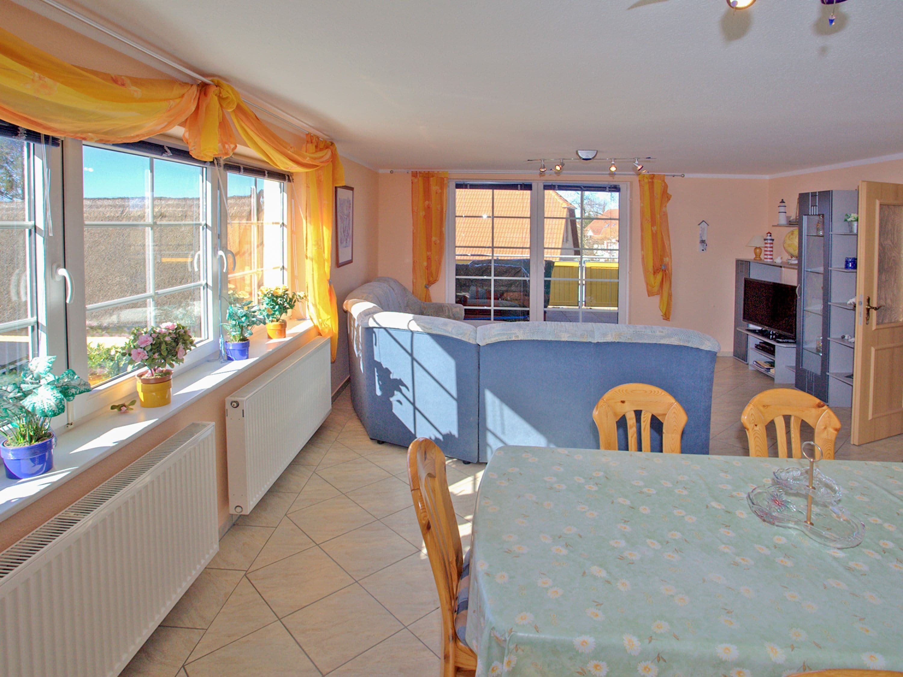A kitchen with a blue countertop, a dining table with a floral tablecloth, and potted plants on the windowsill.