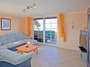 A living room with a sofa, a small table, a TV, and a sliding glass door leading to a balcony. - Vacation Apartment 4 - Villa Lisa (Glowe)