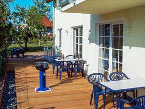 An outdoor patio with a wooden deck, blue plastic chairs, and a table. - Vacation Apartment 4 - Villa Lisa (Glowe)
