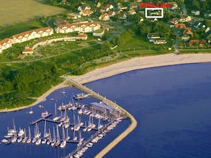 An aerial view of Villa Lisa, featuring a marina with numerous boats, a sandy beach, and surrounding residential buildings. - Vacation Apartment 4 - Villa Lisa (Glowe)