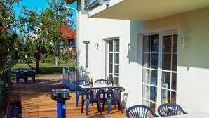 Um pátio externo com deck de madeira, cadeiras de plástico azul e uma mesa.