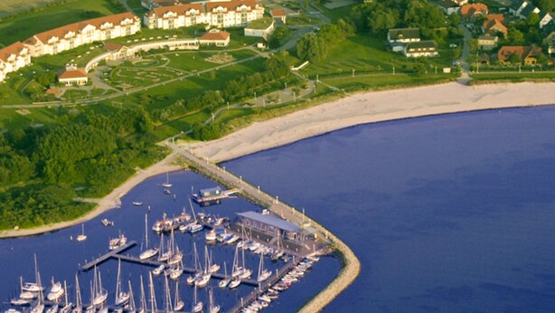 Vista aérea da Villa Lisa, mostrando uma marina com vários barcos, uma praia de areia e edifícios residenciais ao redor.