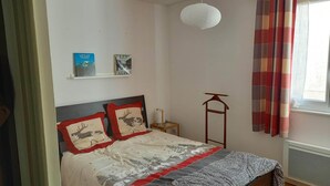 Een slaapkamer met een bed, nachtkastje, hanglamp, radiator en raam met gordijnen.
