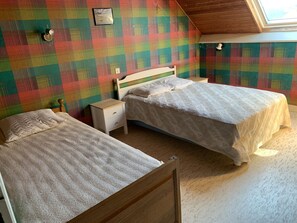 Une chambre avec deux lits, une tête de lit en bois, une petite table de chevet et un mur décoré d’un motif à carreaux coloré.