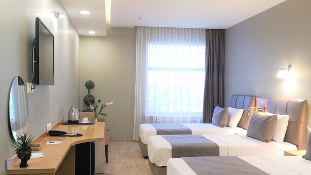 Quarto de hotel com duas camas, uma escrivaninha, uma televisão e uma janela com cortinas.