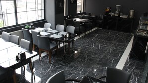 Restaurante moderno com piso de mármore, decoração em preto e branco e amplas janelas com vista para a rua.
