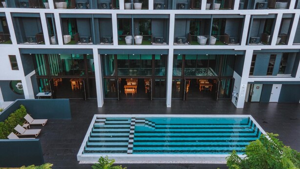 Un hotel moderno con piscina central, varios balcones y zonas de estar al aire libre.