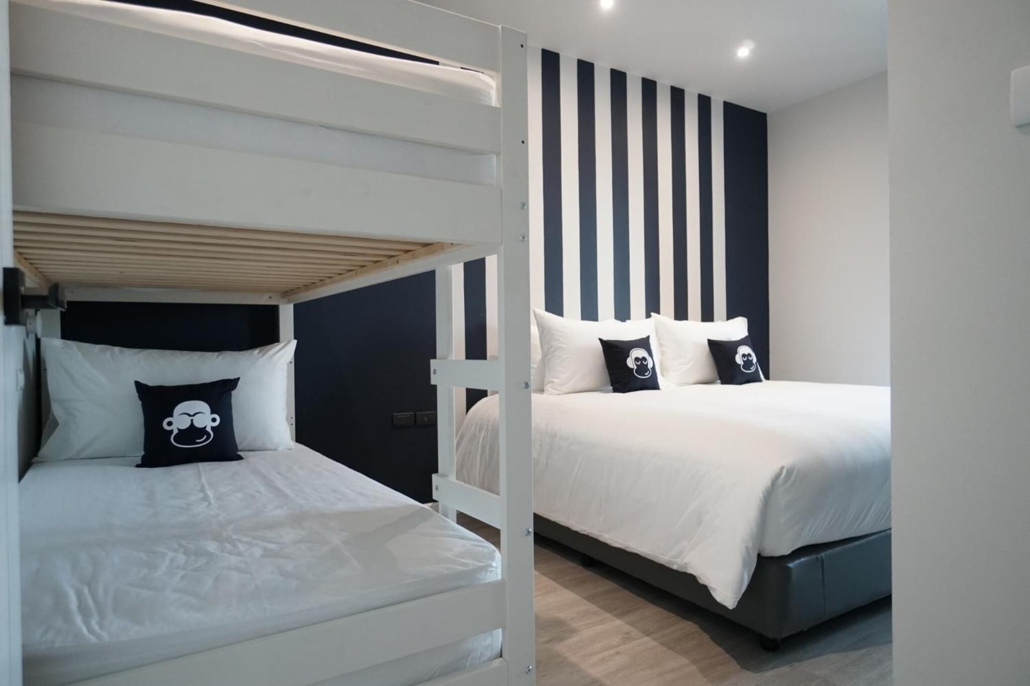 Una habitación con literas y una cama individual, ambas con ropa de cama blanca y almohadas negras.
