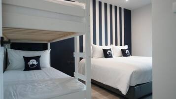 Una habitación con literas y una cama individual, ambas con ropa de cama blanca y almohadas negras.