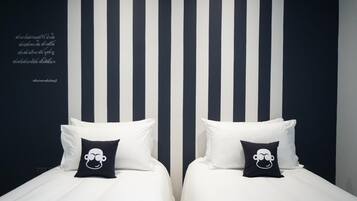 A hotel room with two beds, each with white bedding and black pillows featuring a cartoon character. The room has a striped wall design and a quote in a foreign language.